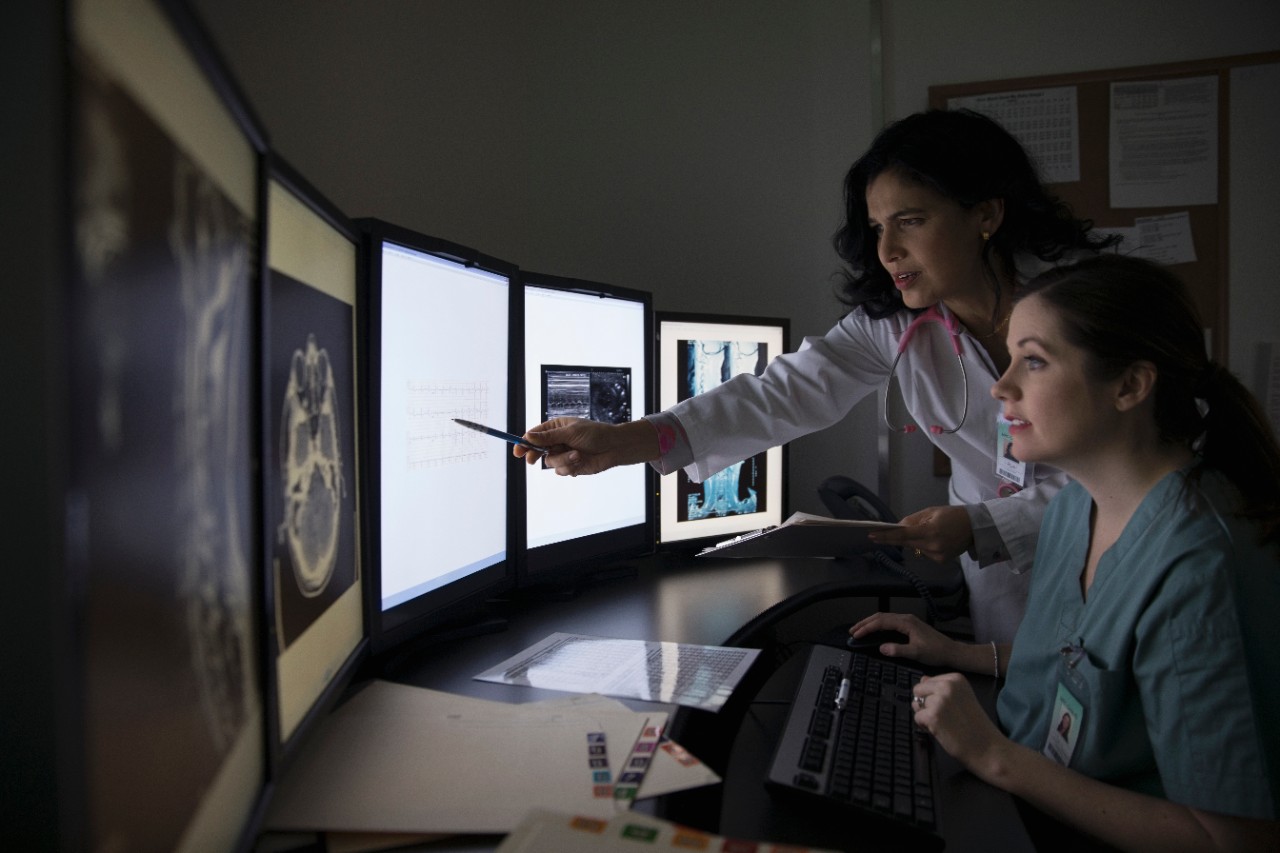 Female doctor and nurse reviewing and discussing digital x-ray on computer in dark room